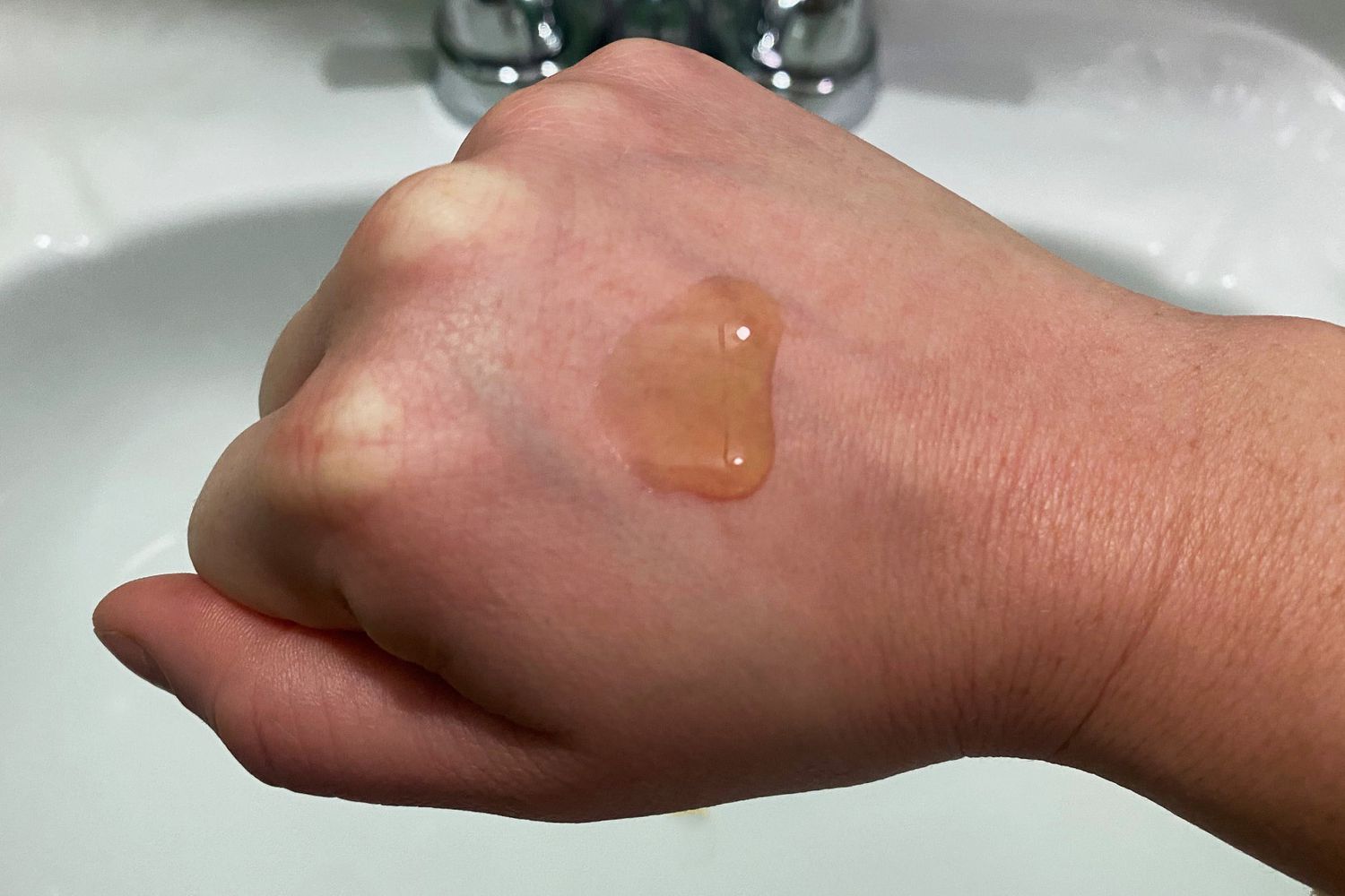 The Paula's Choice Clinical Niacinamide 20% Treatment on the back of a hand hovering over a sink