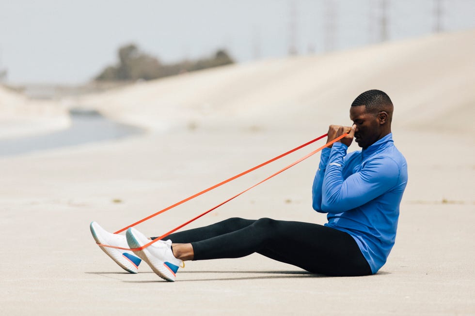 side view of man stretching resistance band while sitting on land during sunny day