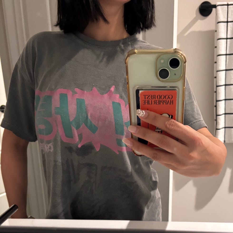 Person wearing a gray t-shirt with graphic text and holding a phone