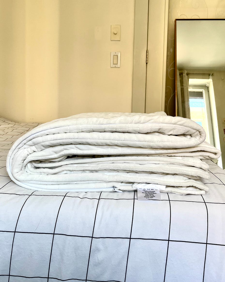 folded white comforter on a bed with a grid patterned weighted blanket and a mirror in the background