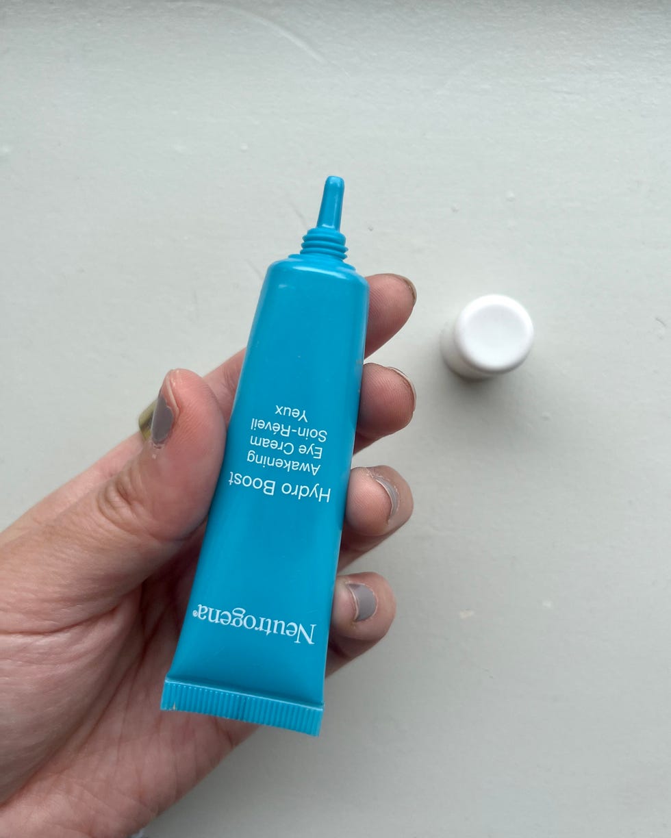 a blue tube of eye cream held in a hand with a white cap nearby