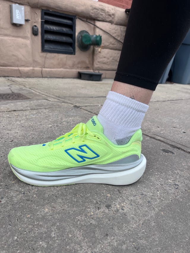 Bright green athletic shoe worn with white socks on a sidewalk.