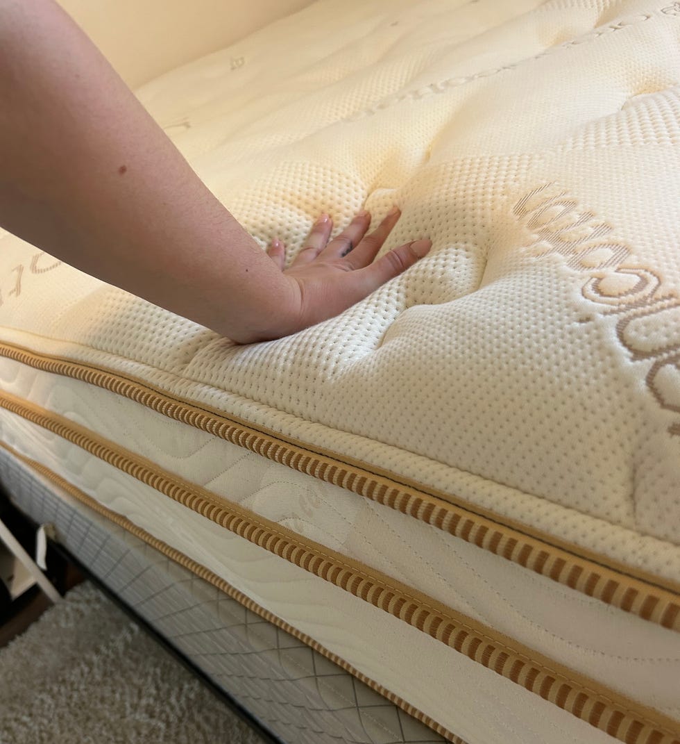 a hand pressing down on a saatva classic mattress