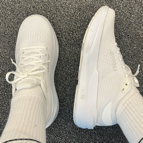 White running shoes with a textured surface and laces, paired with white socks featuring black stripes.