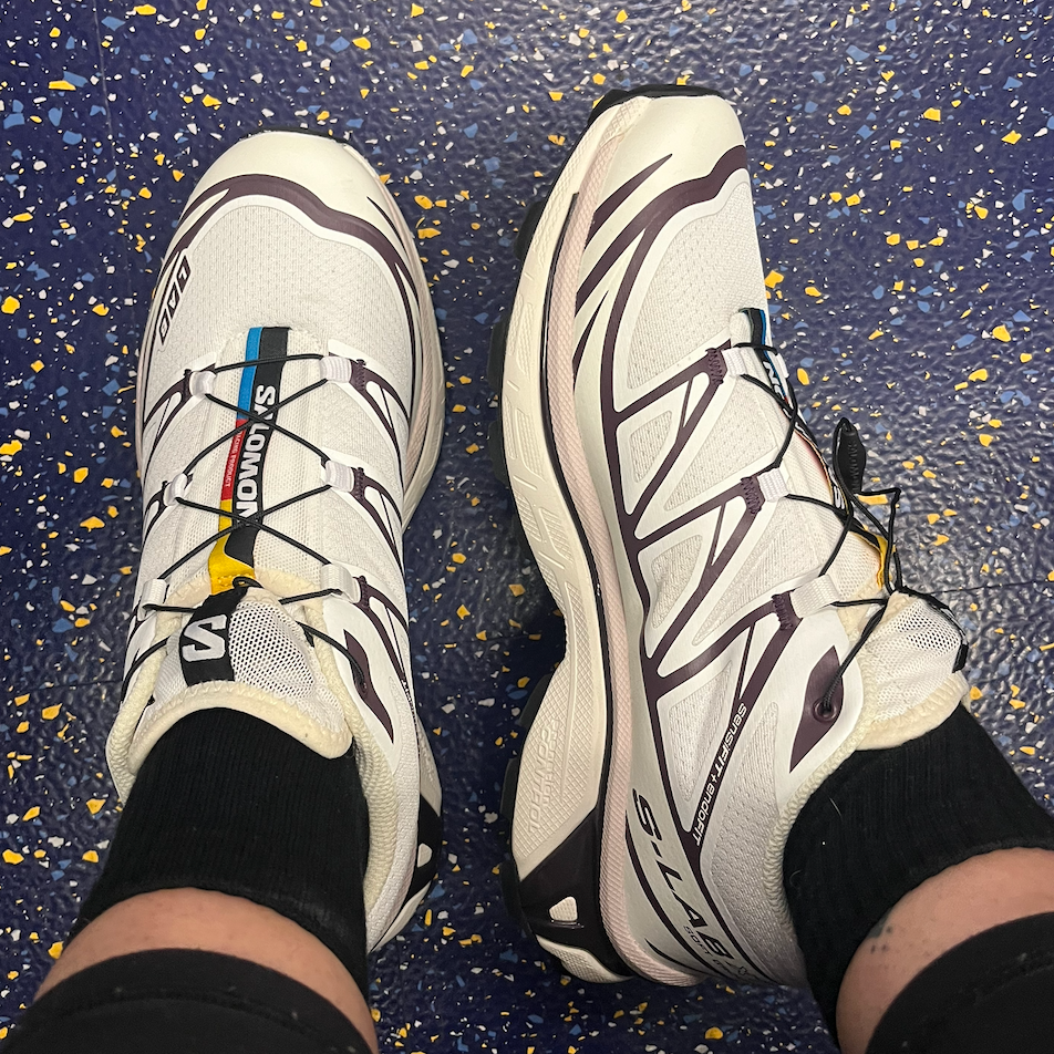 Pair of white athletic shoes on a blue and yellow speckled floor.