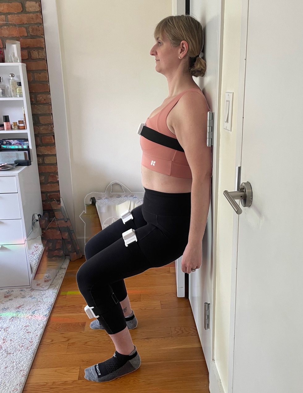Person performing an exercise against a wall with equipment attached.