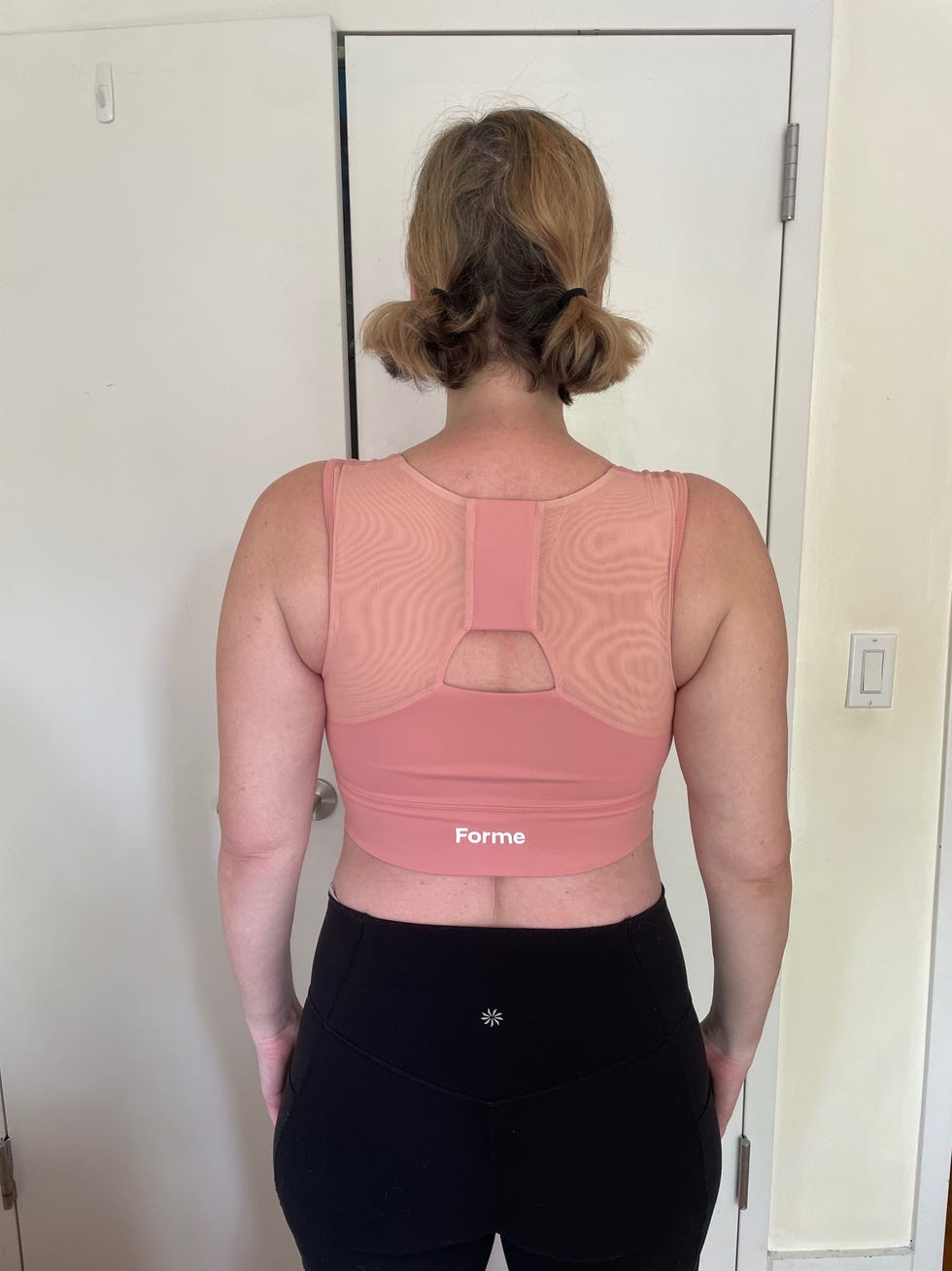 Woman wearing a pink athletic top and black leggings, viewed from the back.