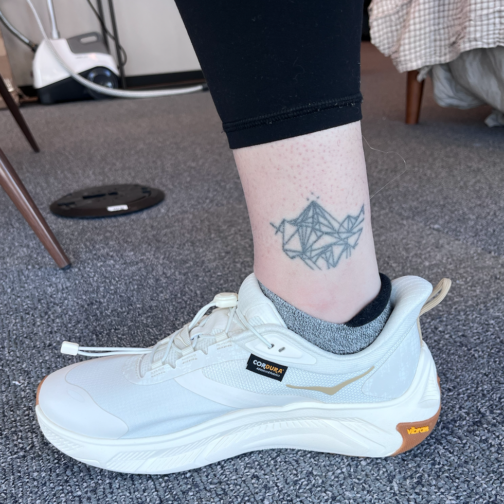 Sport shoe worn on a leg with a decorative tattoo.