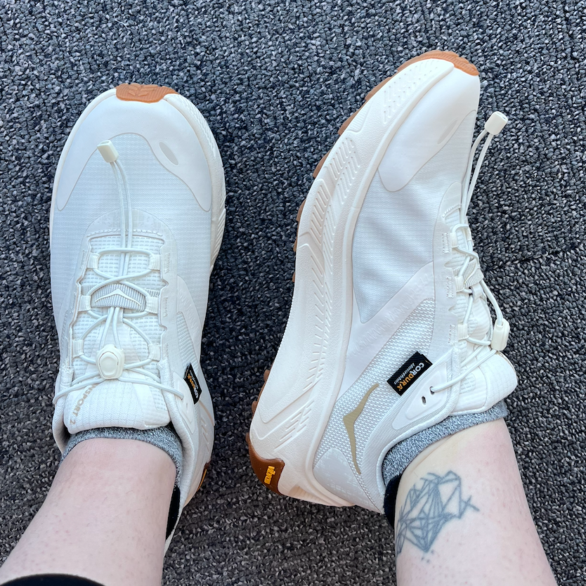 White athletic shoes worn by a person with a tattoo on their ankle.