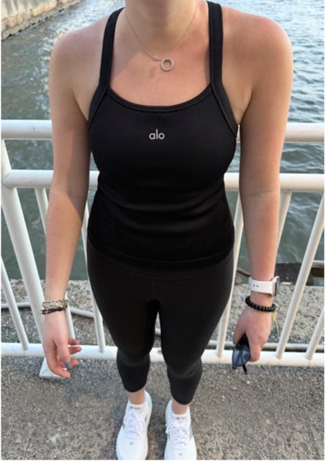 A person wearing a black athletic outfit by Alo standing near a water body.