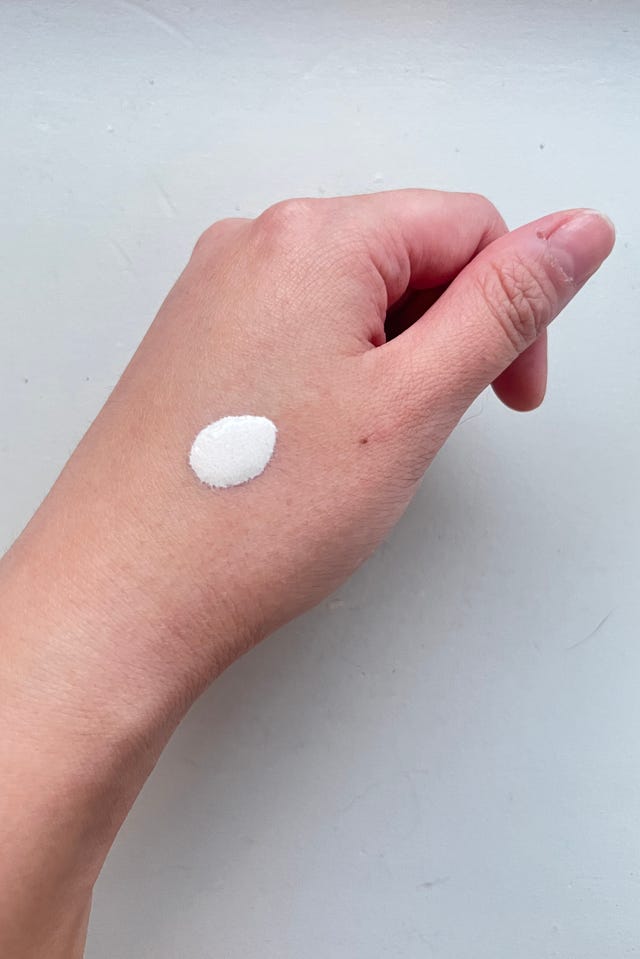 Hand applying a white substance on the skin.