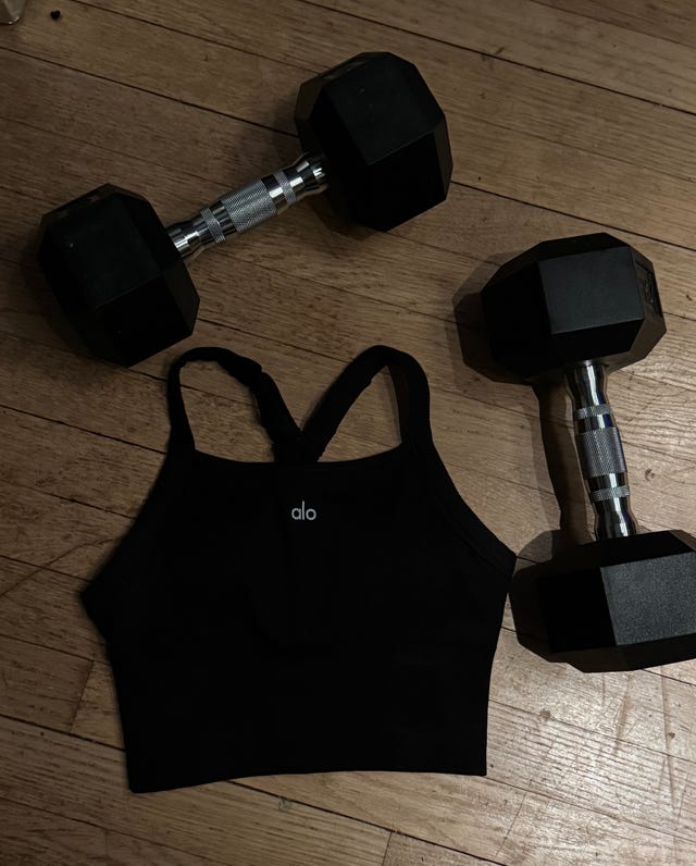 Black sports bra with dumbbells on a wooden floor.