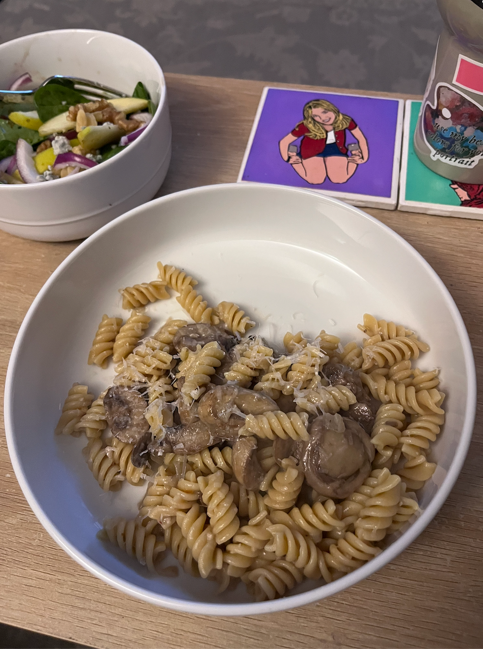 A bowl of pasta with mushrooms and grated cheese alongside a salad and coasters.