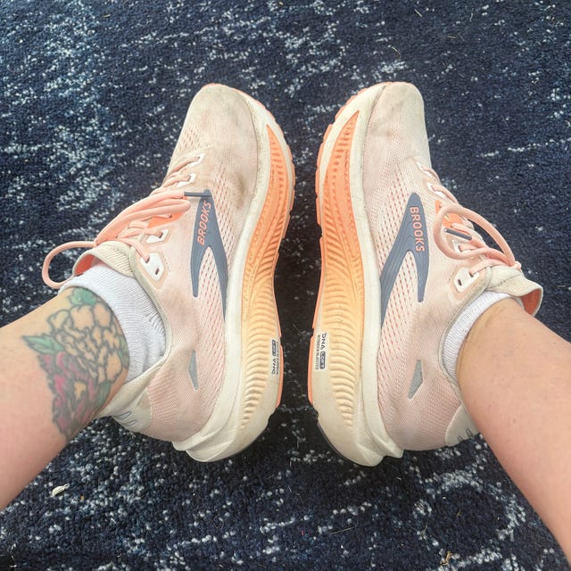 Person wearing light peach running shoes with orange soles on a blue patterned carpet.