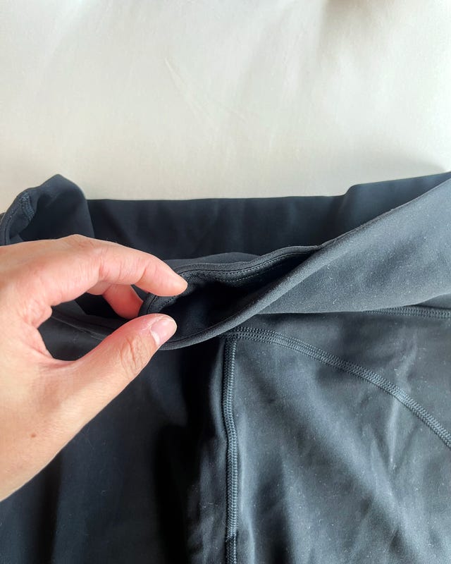 Hand holding the waistband of black pants demonstrating pocket feature.