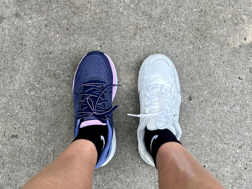 Two different sneakers, one navy blue and one white, worn on opposite feet, displayed on a concrete surface.