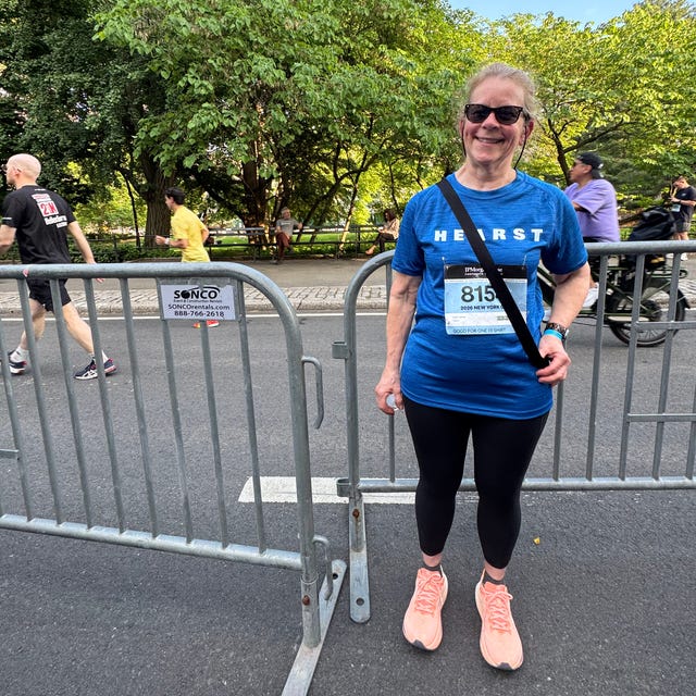 Smiling woman in blue shirt and sunglasses standing by a barricade at a park event.