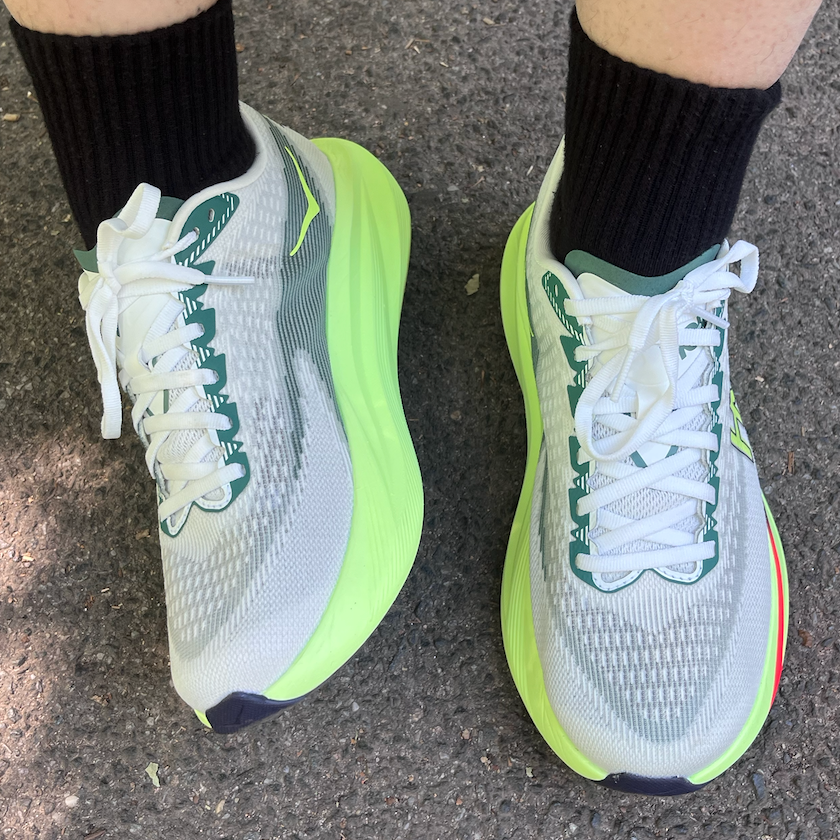Person wearing white sneakers with neon green soles on pavement.