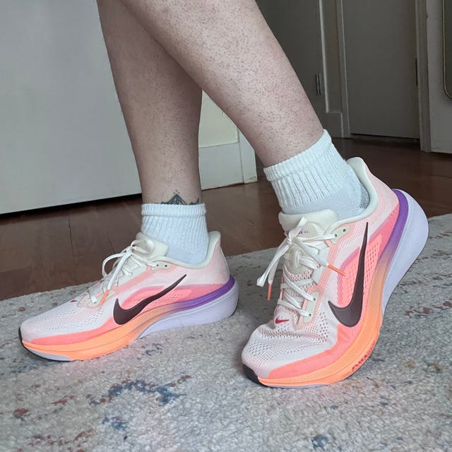 Person wearing white and orange Nike running shoes indoors on patterned carpet.