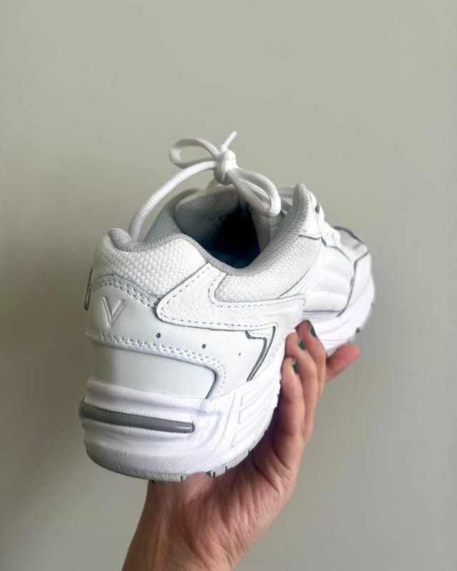 White athletic shoe held in a hand, showcasing the back view with a tied shoelace.