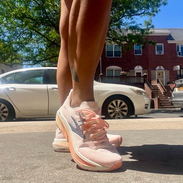 Person wearing light pink running shoes standing on a street sidewalk.