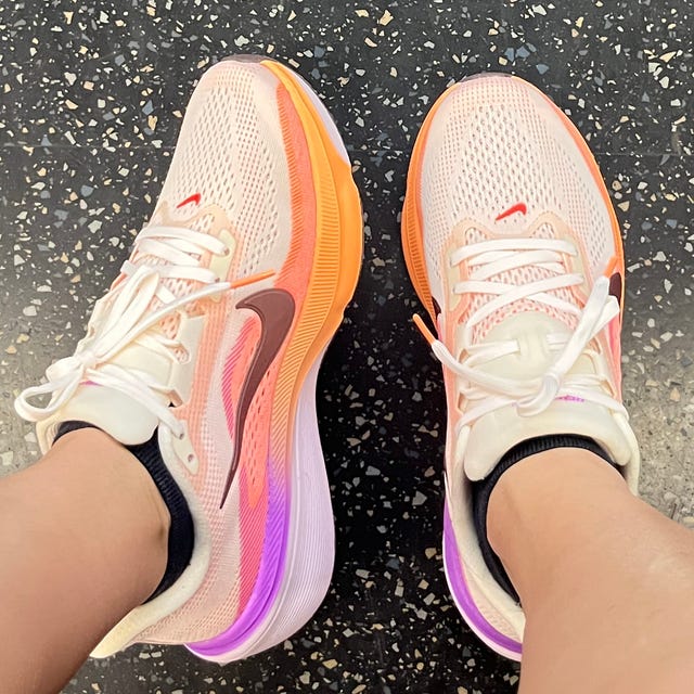 Pink and orange Nike running shoes on speckled floor.