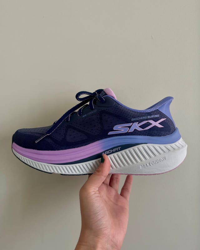 Navy and pink Skechers running shoe held by a hand against a light wall background.