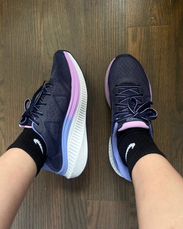 A pair of navy and purple running shoes worn with black socks on a wooden floor.