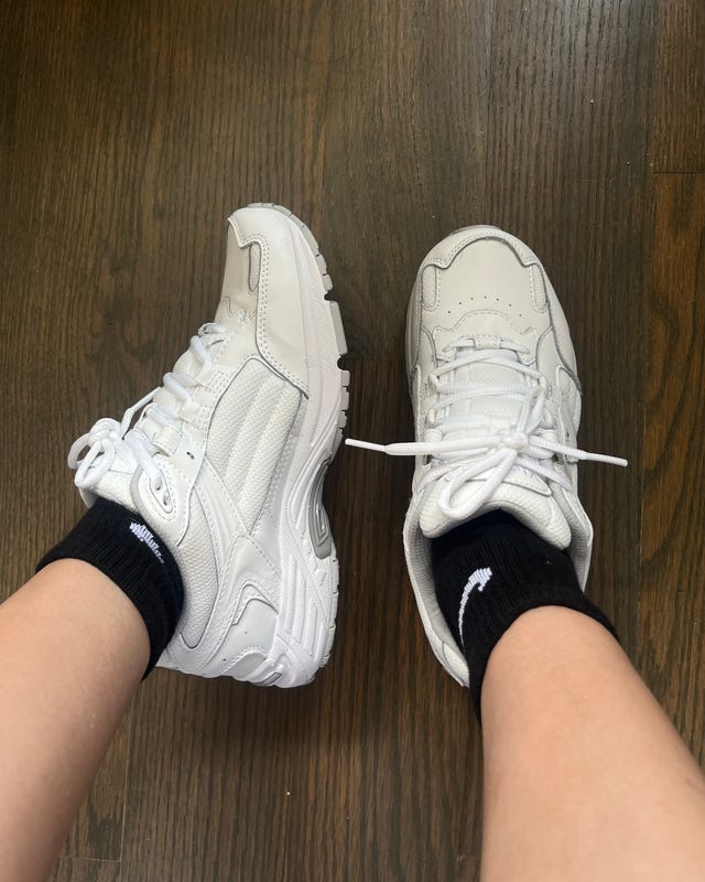 White athletic shoes paired with black socks on a wooden floor.