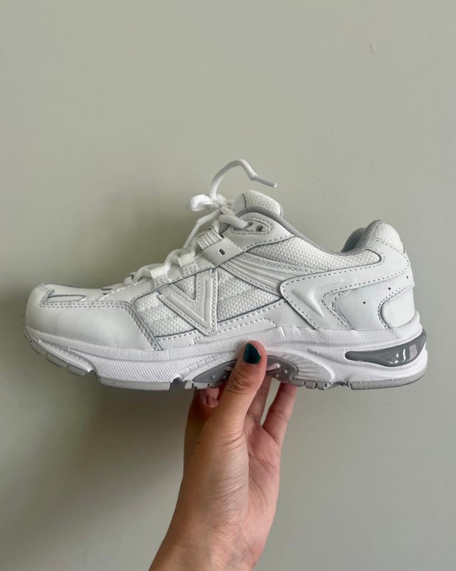 White sneaker held in one hand against a neutral background.