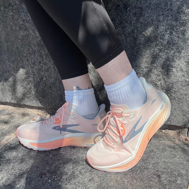 Person wearing peach running shoes, black leggings, and white socks sitting on a stone surface.