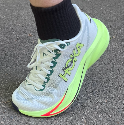 Person wearing bright green and white running shoes on a sidewalk.