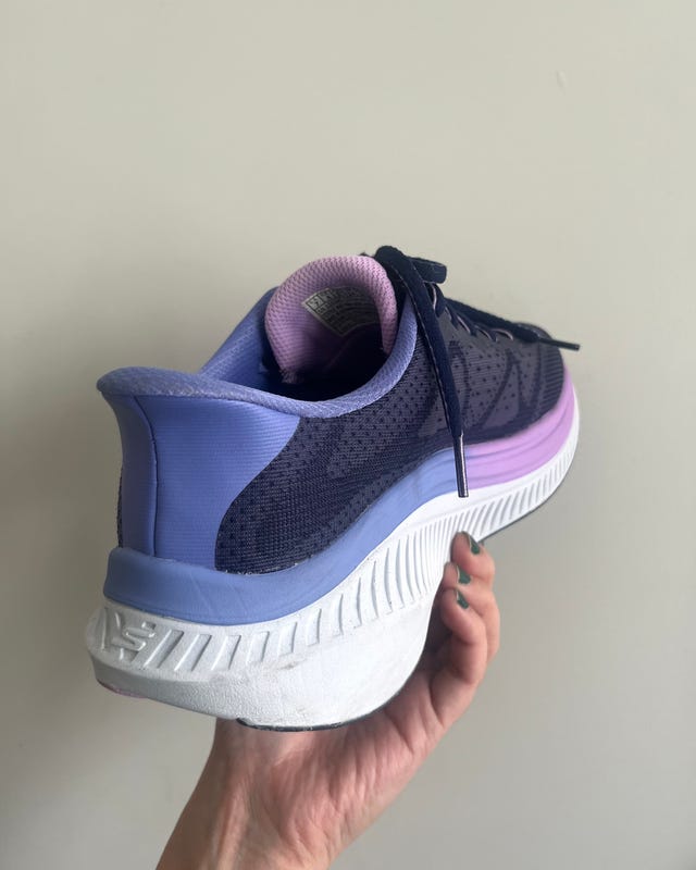 Close-up of a women's running shoe in navy blue and purple, held against a neutral background.