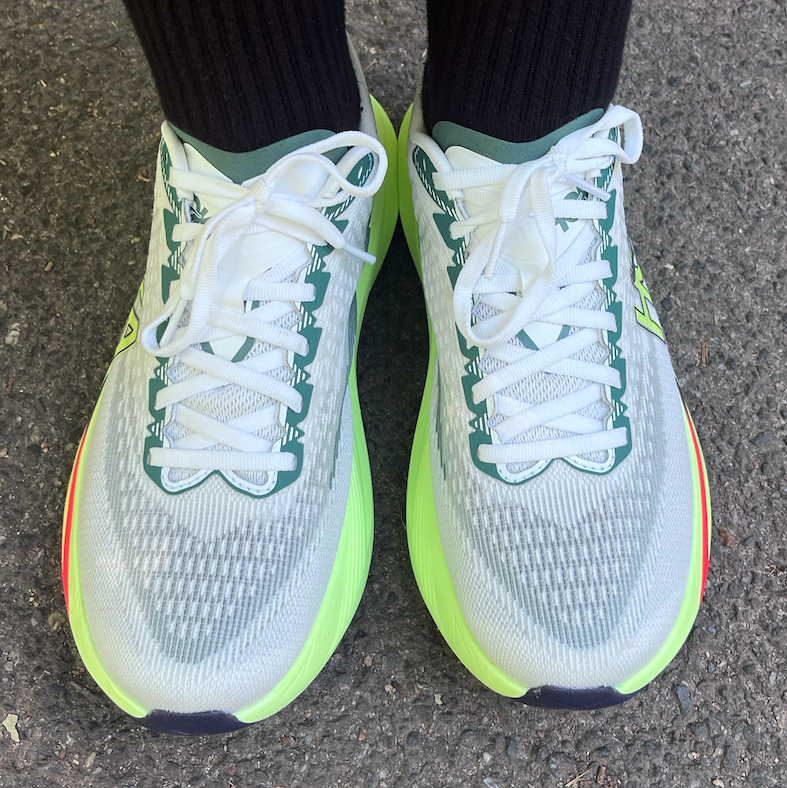 White and neon green running shoes on pavement with black socks
