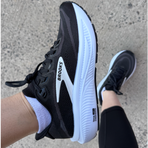 Person wearing black Brooks running shoes on concrete surface.