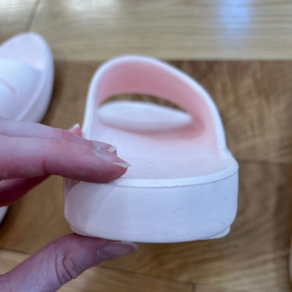 Close-up of a hand holding a pink slide sandal, focusing on the side view and detailing of the shoe's structure.
