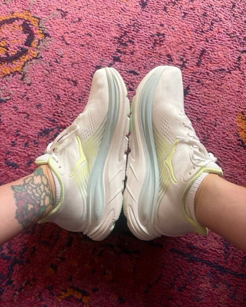 Light-colored athletic shoes on feet, positioned on a patterned pink rug. Light-colored athletic shoes on feet, positioned on a patterned pink rug.