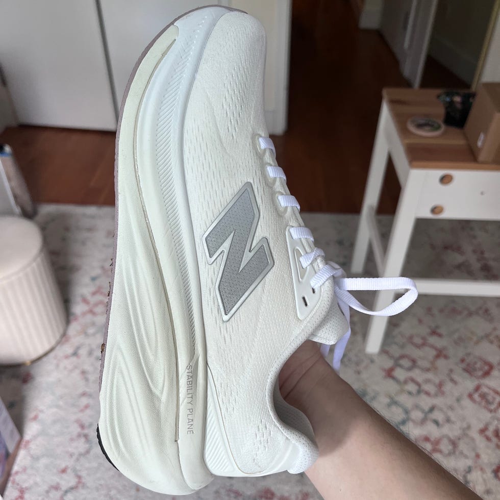 White athletic shoe with gray logo, held sideways above a patterned rug.