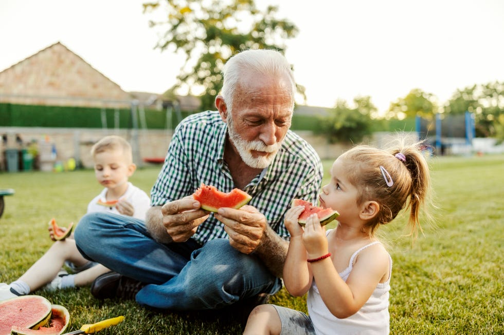happy children with granddad sitting on a lawn in backyard and enjoying watermelon