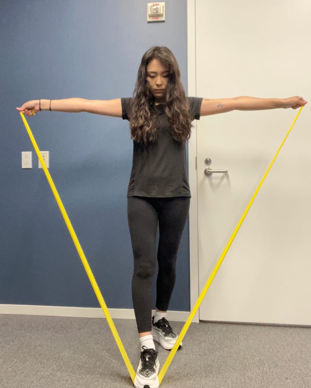 Person performing a resistance band exercise with arms extended in a V shape against a blue wall.