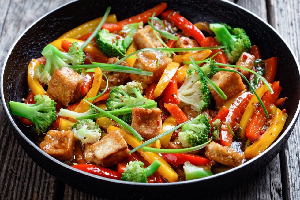 close up of kung pao tofu with mixed peppers, broccoli and scallions in a skillet on a rustic wooden table, chinese cuisine, landscape view from above