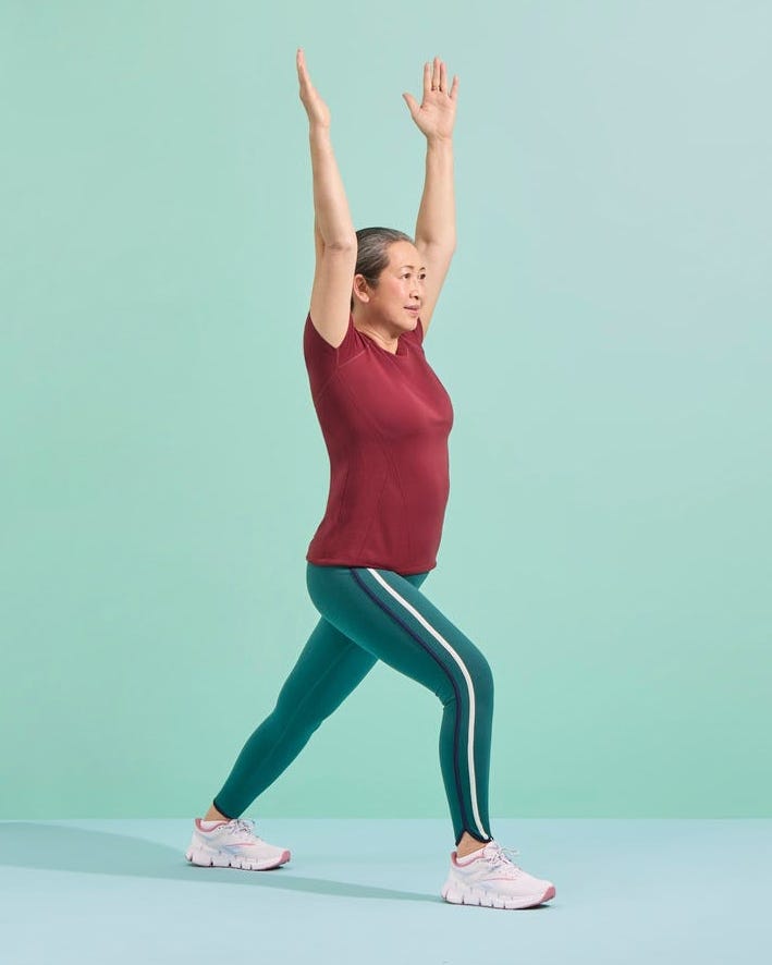 A woman in workout attire demonstrates a yoga pose with her arms raised against a light green background.