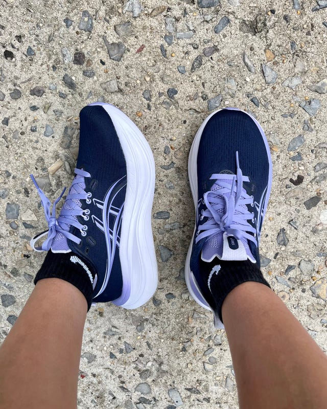 A pair of athletic shoes with purple accents and black Nike socks on a textured concrete surface.