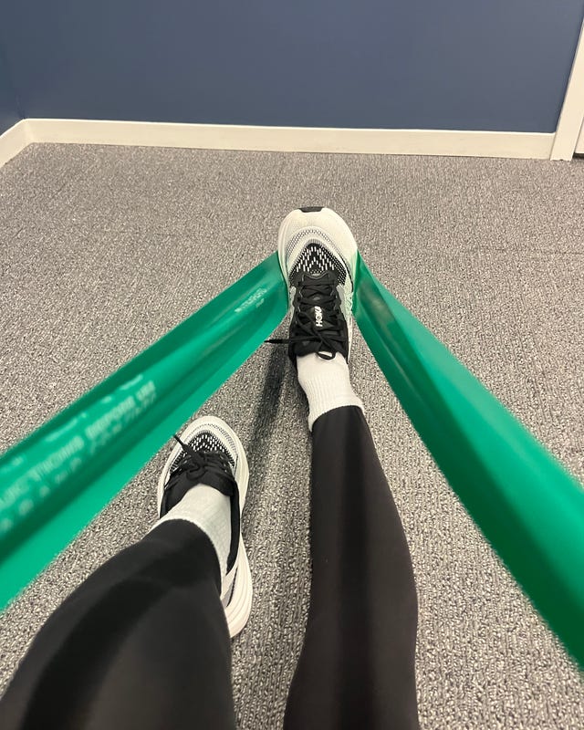 Person's legs in athletic wear using resistance bands on a gym floor with a blue wall backdrop.