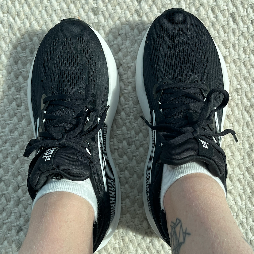 Top view of black athletic shoes worn with white socks on a textured light-colored rug.