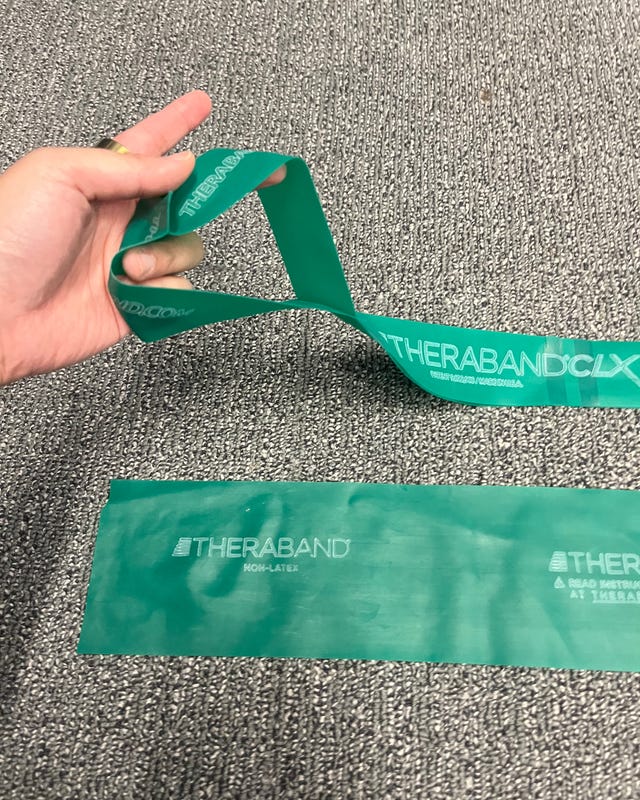 Green resistance band from Theraband, held in a hand, lying on a textured surface.