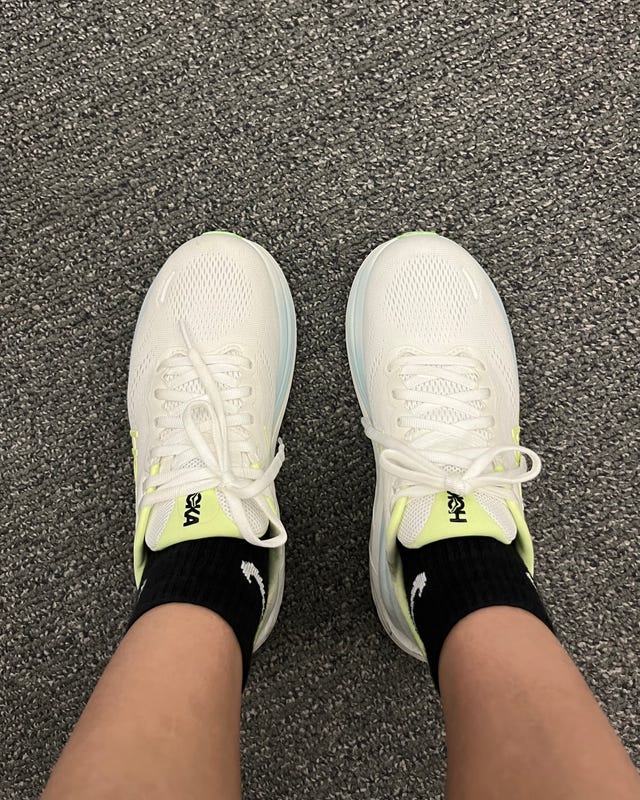 White athletic shoes with neon accents worn with black socks on a textured gray carpet. White athletic shoes with neon accents worn with black socks on a textured gray carpet.