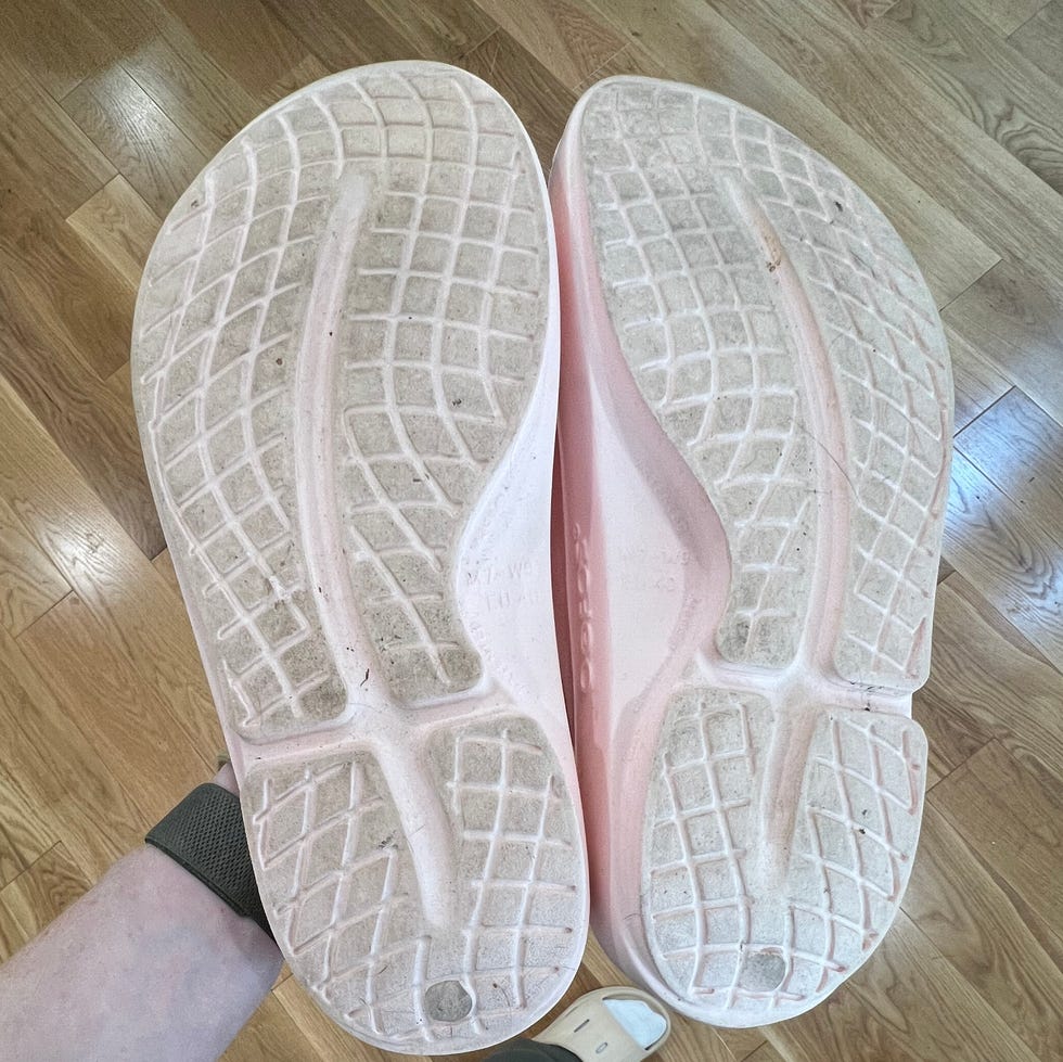 A person holding pink-soled shoes over their feet, standing on a wooden floor.