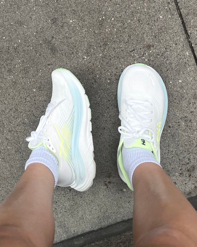 White athletic shoes with light green accents worn with ankle socks, positioned on a concrete surface. White athletic shoes with light green accents worn with ankle socks, positioned on a concrete surface.