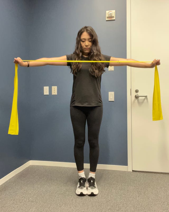 Person performing a resistance band exercise with arms extended in a fitness studio.